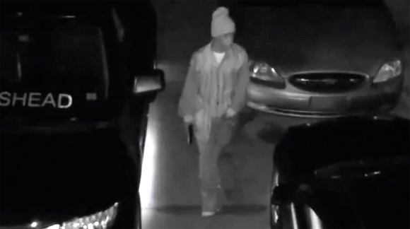One of the suspects, a black male, walks onto the driveway with a handgun and checks the door handles on the vehicle. (Palm Bay police video image)