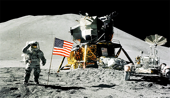   Jim Irwin, Apollo 15 lunar module driver greets the American flag 1, 1971. The lunar module, Falcon, is visible on the right. Irwin and Mission Commander David Scott were among the 12 Americans to walk on the moon between July 1969 and December 1972. 