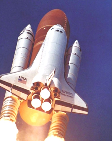 With the Hubble Space Telescope on board, Discovery begins its roll maneuver after liftoff from Kennedy Space Center on April 24, 1990. This low-angle view of the launch shows the shuttle atop the external tank, flanked by two solid rocket boosters, as it rises into the sky.