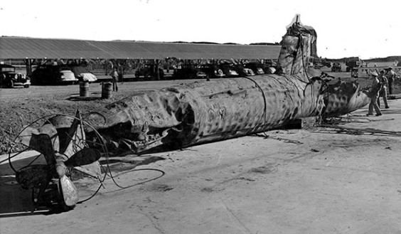 A Japanese midget submarine is salvaged and later buried in a landfill after being sunk by USS Monaghan during the Pearl Harbor attack. The sub’s hull shows the effects of depth charges and ramming. A hole visible in the after part of the conning tower may be from a five shell. The upper background had been painted over for censorship purposes. (Department of Defense image)