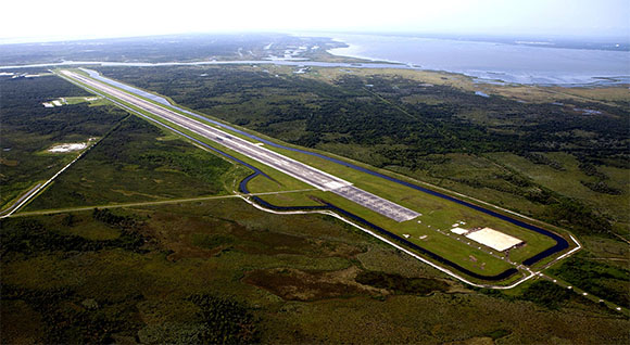 This aerial photo of the Shuttle Landing Facility runway at the Kennedy Space Center looks southwest. Longer and wider than most commercial runways, it is 15,000 feet long, with 1,000-foot paved overruns on each end, and 300 feet wide, with 50-foot asphalt shoulders. The property agreement with Space Florida for the operations and management will allow a variety of commercial and government partners to use the three-mile long runway. (NASA.gov image)