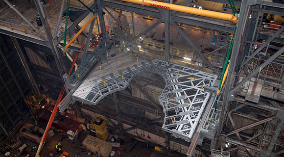 Inside the Vehicle Assembly Building at NASA's Kennedy Space Center in Florida, the 325-ton crane lifts the first half of the K-level work platforms up for installation in High Bay 3 on Dec. 22. The platform will be secured into position on tower E, about 86 feet above the floor. The K work platforms will provide access to NASA's Space Launch System (SLS) core stage and solid rocket boosters during processing and stacking operations on the mobile launcher. (NASA.gov image)